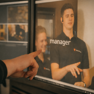 Hand wijst naar computerscherm met videobewerking waarop een medewerker in beeld is, illustratief voor een bedrijfsfilm laten maken.
