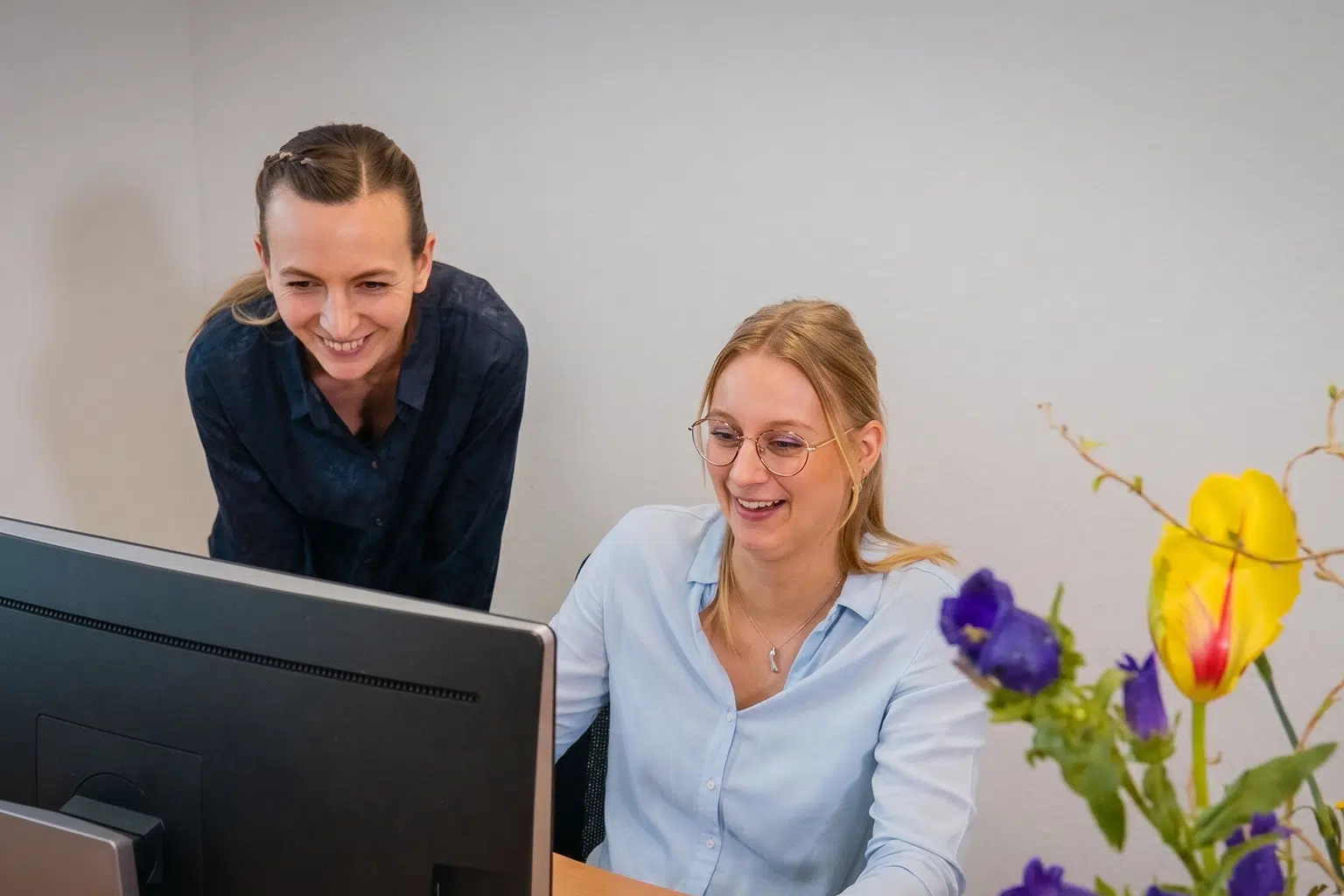 Twee mensen werken samen achter een computer in een lichte kantoorruimte.