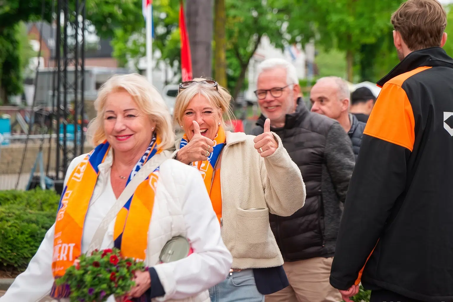 Groep mensen met oranje en blauwe sjaals tijdens een feestelijke buitenbijeenkomst.